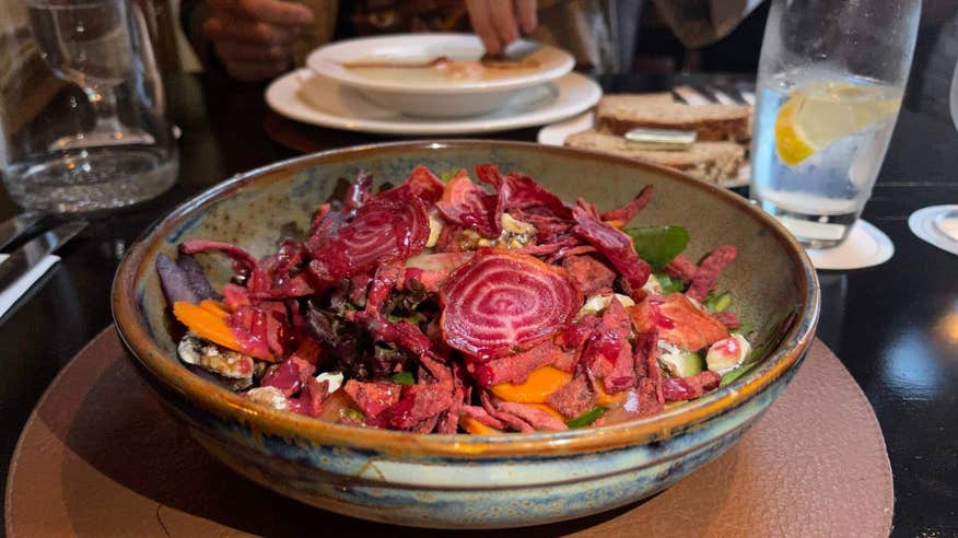 A photo of a vegan salad with deep red beets, bright orange carrots, and other vegetables chopped up in a bowl.