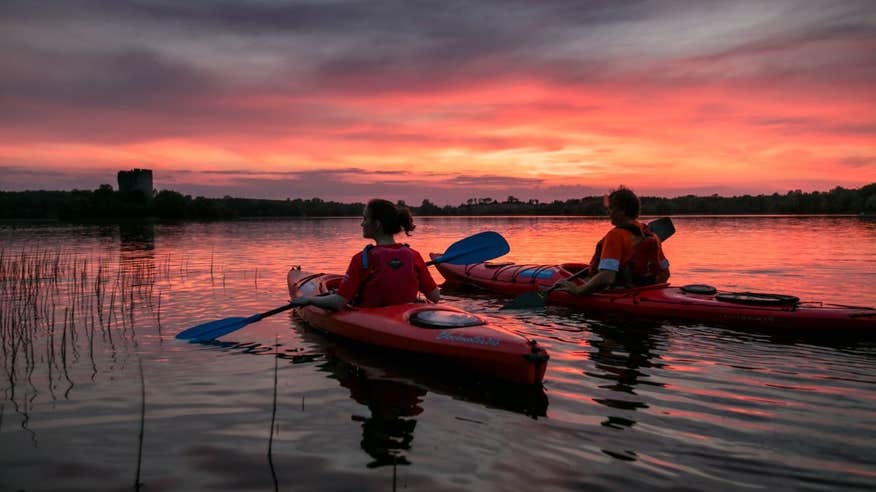 People kayaking through still waters with beautiful sunset views
